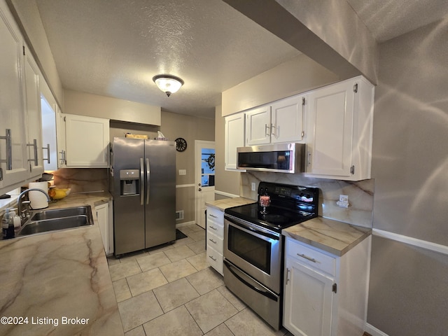 kitchen featuring a sink, a textured ceiling, decorative backsplash, white cabinets, and appliances with stainless steel finishes