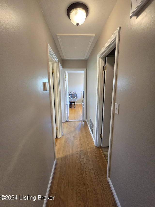 hall featuring attic access, baseboards, wood finished floors, and visible vents