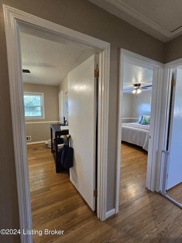 corridor featuring wood finished floors, visible vents, baseboards, and ornamental molding