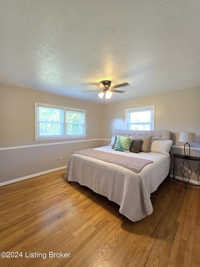 bedroom featuring multiple windows, wood finished floors, and a textured ceiling