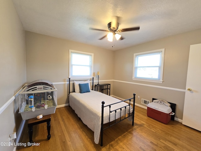 bedroom with baseboards, wood finished floors, visible vents, and a textured ceiling
