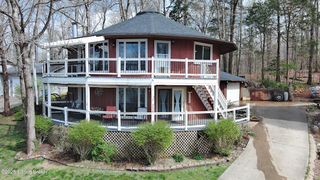 back of house with concrete driveway, a shingled roof, covered porch, a garage, and stairs