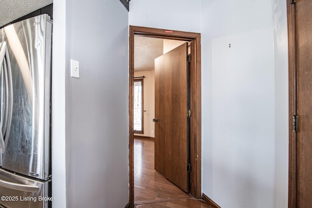 corridor featuring baseboards, wood finished floors, and a textured ceiling