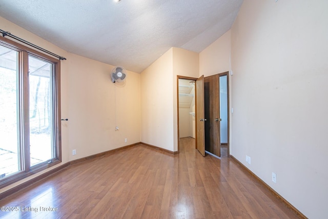 unfurnished room with vaulted ceiling, a textured ceiling, wood finished floors, and plenty of natural light