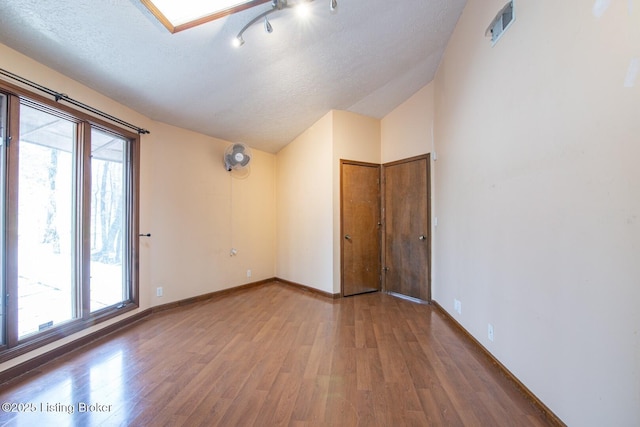 unfurnished room with wood finished floors, visible vents, a textured ceiling, and vaulted ceiling with skylight