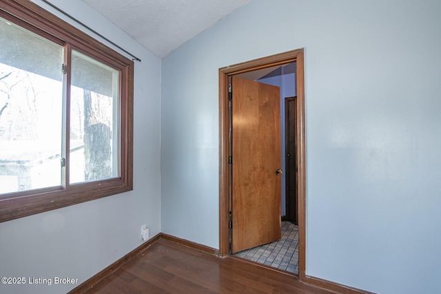 empty room with lofted ceiling, baseboards, wood finished floors, and a textured ceiling