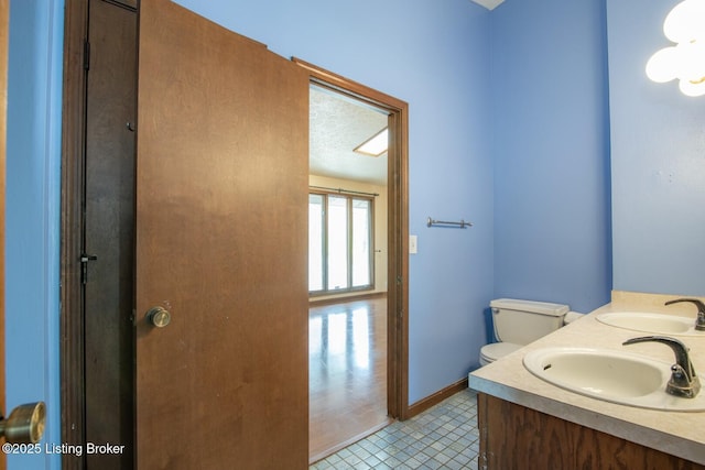 bathroom featuring double vanity, toilet, baseboards, and a sink