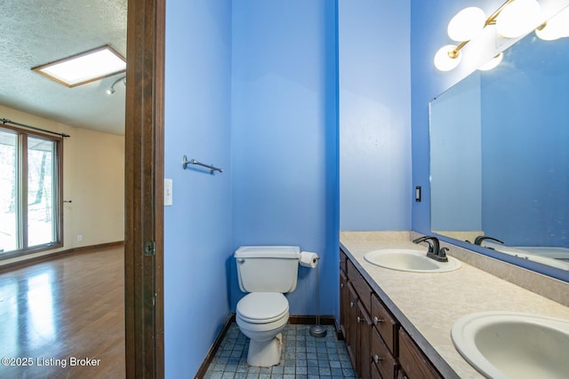 bathroom with a textured ceiling, toilet, baseboards, and a sink