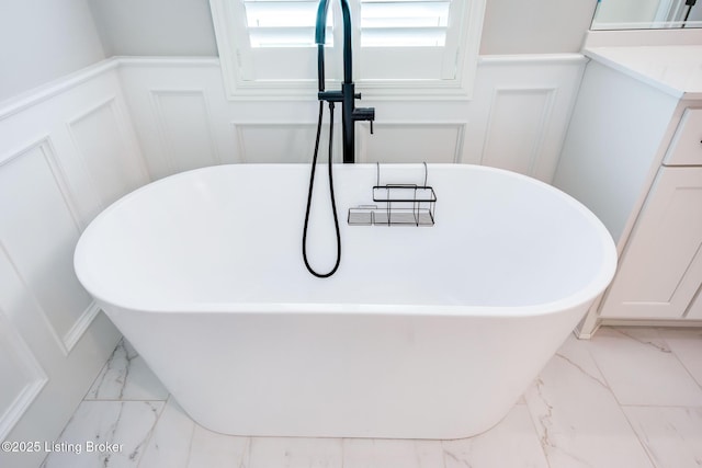 details featuring wainscoting, a freestanding tub, vanity, and a decorative wall