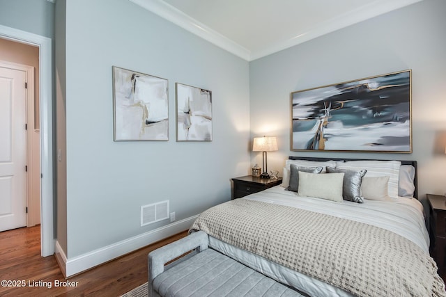 bedroom with baseboards, wood finished floors, visible vents, and ornamental molding