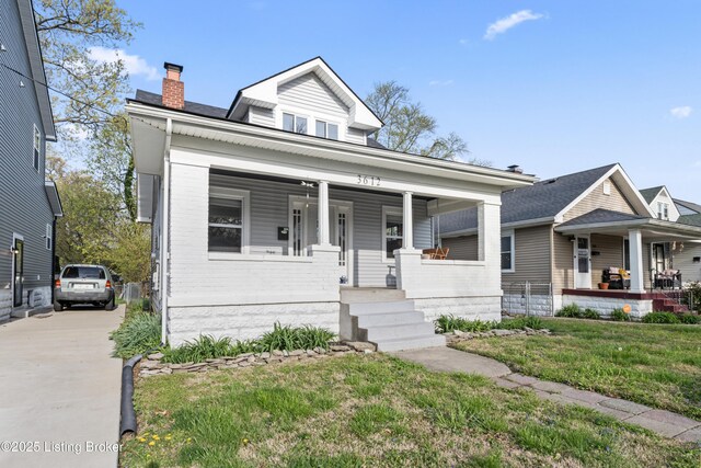 view of front of house featuring a chimney, a front lawn, driveway, a porch, and brick siding