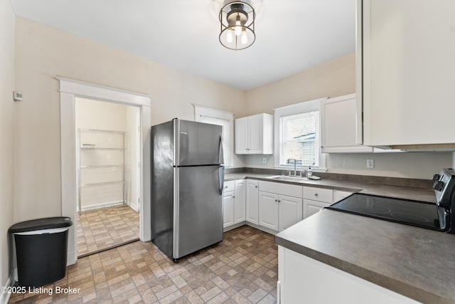 kitchen featuring dark countertops, a sink, electric range, brick patterned floor, and freestanding refrigerator