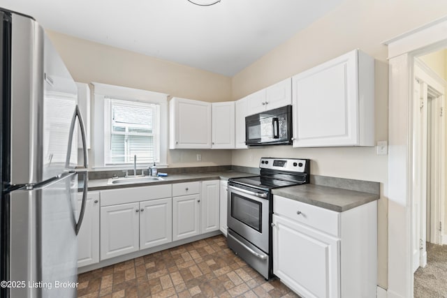 kitchen with white cabinets, dark countertops, a sink, and appliances with stainless steel finishes