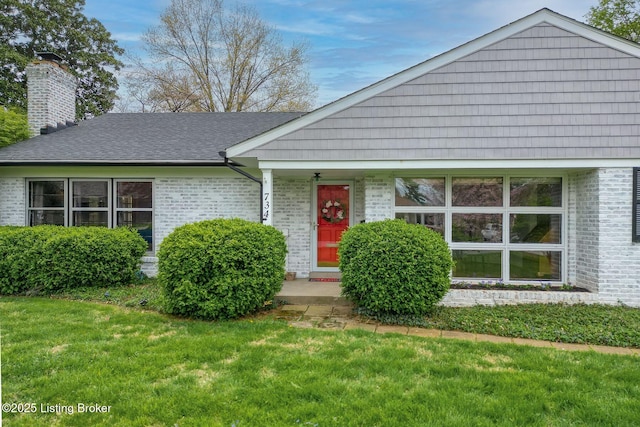 single story home with a front lawn, brick siding, roof with shingles, and a chimney