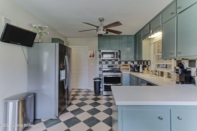 kitchen with stainless steel appliances, a peninsula, tile patterned floors, a sink, and ceiling fan