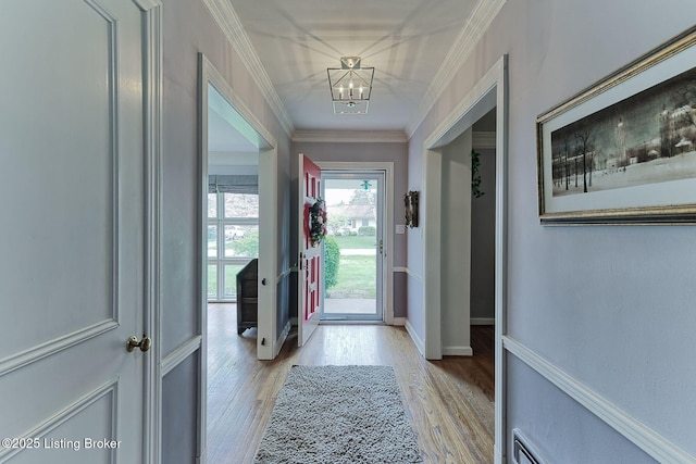 doorway to outside featuring light wood-style floors, crown molding, baseboards, and an inviting chandelier
