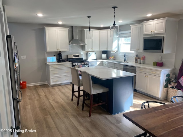 kitchen with wall chimney exhaust hood, white cabinetry, stainless steel appliances, and light wood finished floors