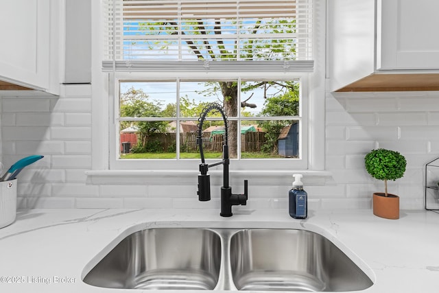 interior details featuring white cabinetry, light stone counters, a sink, and tasteful backsplash