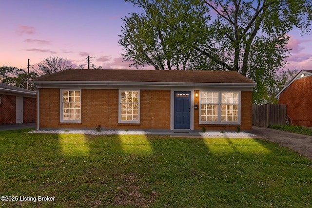view of front of house featuring brick siding, fence, and a yard