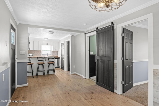 kitchen with white cabinets, a kitchen bar, a barn door, light wood-style flooring, and ornamental molding