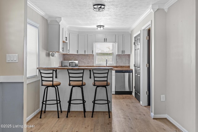 kitchen with stainless steel appliances, a peninsula, a kitchen bar, decorative backsplash, and light wood-type flooring