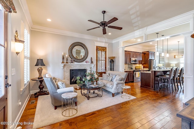 living room with crown molding, a tiled fireplace, a ceiling fan, and dark wood-style flooring