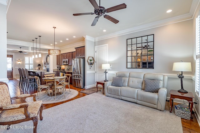 living area with crown molding, wood finished floors, ceiling fan, a wainscoted wall, and recessed lighting