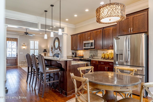 kitchen featuring stainless steel appliances, a ceiling fan, ornamental molding, light stone countertops, and a kitchen island with sink