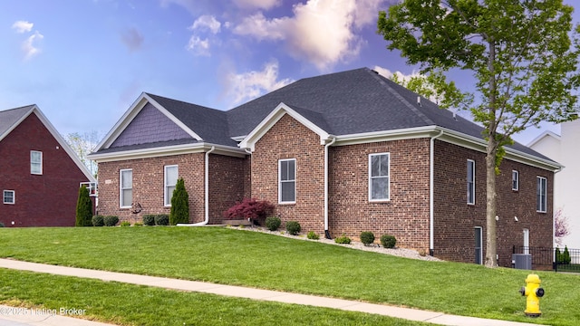 view of front of home featuring fence, roof with shingles, a front yard, and brick siding
