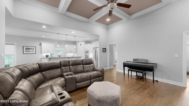 living area with coffered ceiling, a ceiling fan, beam ceiling, and wood finished floors