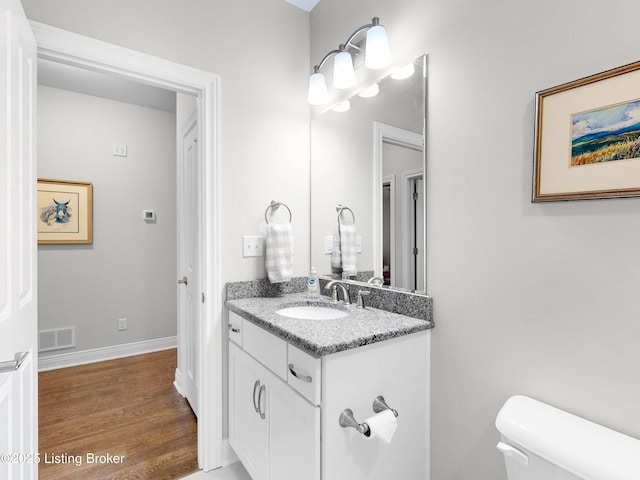 bathroom with vanity, toilet, visible vents, baseboards, and wood finished floors