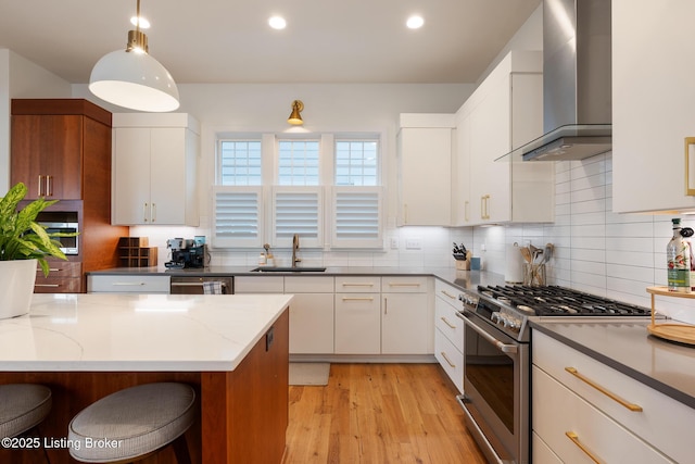 kitchen featuring light wood-style flooring, a sink, dark stone counters, wall chimney range hood, and appliances with stainless steel finishes