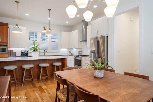 kitchen with wall chimney exhaust hood, a sink, decorative backsplash, appliances with stainless steel finishes, and a breakfast bar area
