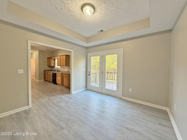 unfurnished living room with light wood finished floors, a raised ceiling, visible vents, and baseboards