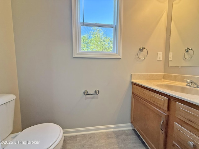 bathroom with toilet, wood finished floors, vanity, and baseboards