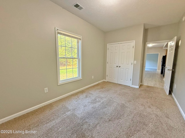 unfurnished bedroom featuring light colored carpet, a closet, baseboards, visible vents, and a textured ceiling