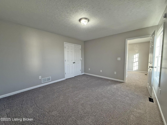 carpeted empty room with a textured ceiling, visible vents, and baseboards