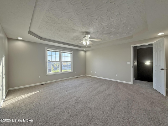 spare room with a raised ceiling, a ceiling fan, carpet flooring, and baseboards