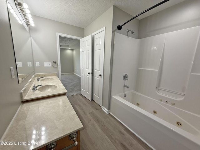 bathroom featuring a combined bath / shower with jetted tub, wood finished floors, double vanity, a sink, and a textured ceiling