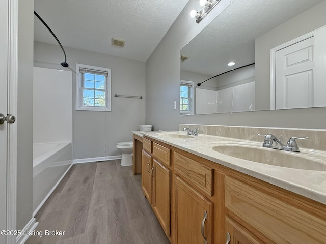bathroom with toilet, a sink, wood finished floors, and visible vents