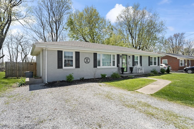 single story home featuring brick siding, fence, a shingled roof, and a front yard