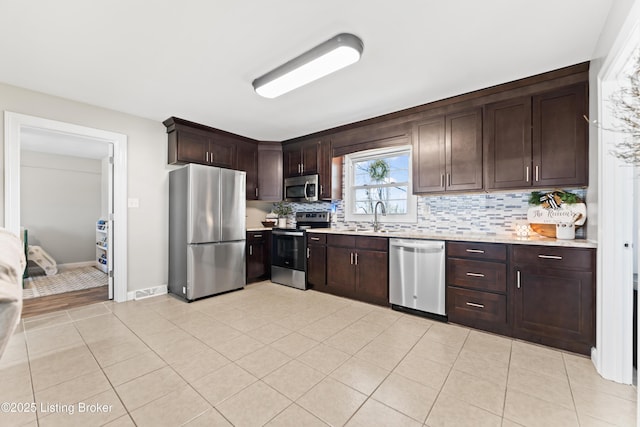 kitchen with tasteful backsplash, dark brown cabinets, a sink, light countertops, and appliances with stainless steel finishes