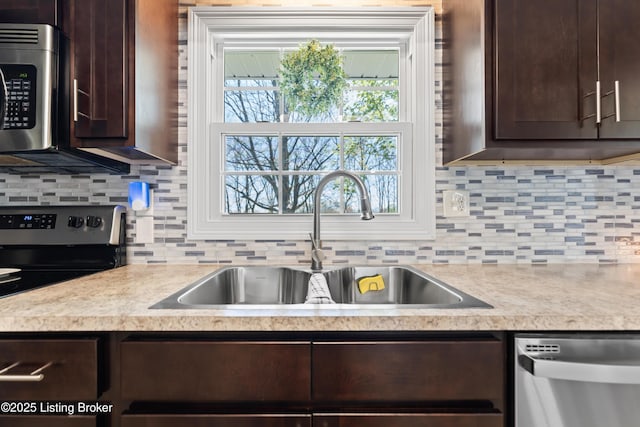 kitchen with dark brown cabinetry, stainless steel appliances, light countertops, and a sink