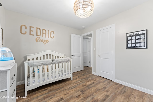 bedroom with wood finished floors, a crib, baseboards, and a notable chandelier