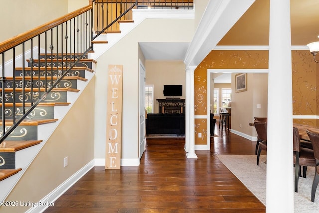 staircase featuring hardwood / wood-style floors, decorative columns, a towering ceiling, a fireplace, and baseboards