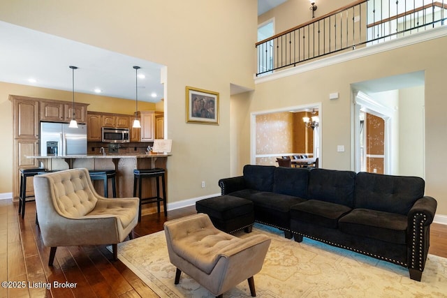 living area featuring a high ceiling, baseboards, hardwood / wood-style floors, and a notable chandelier