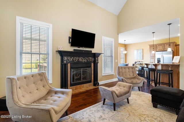 living room with a tiled fireplace, wood finished floors, baseboards, and high vaulted ceiling
