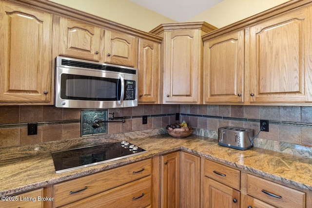 kitchen featuring light stone counters, decorative backsplash, stainless steel microwave, and black electric stovetop