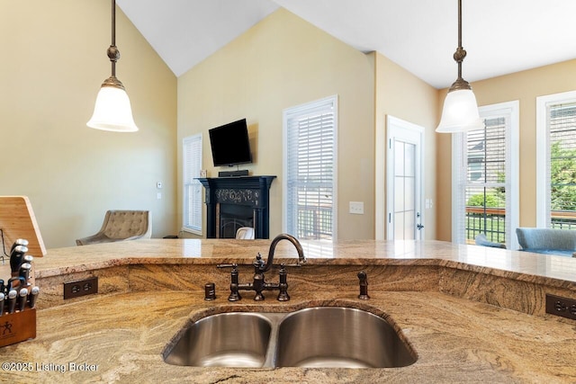kitchen with a fireplace, light stone countertops, pendant lighting, and a sink