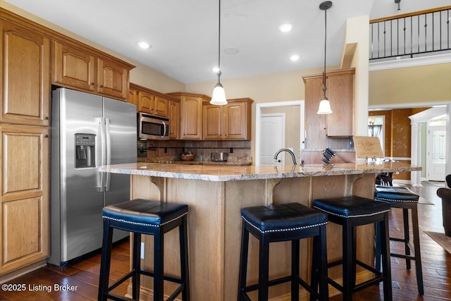 kitchen with a breakfast bar area, dark wood finished floors, light stone countertops, appliances with stainless steel finishes, and tasteful backsplash